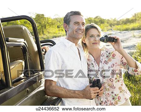 Couple standing by jeep holding binoculars smiling View Large Photo Image Stock Image - Couple standing by jeep holding binoculars smiling. Fotosearch