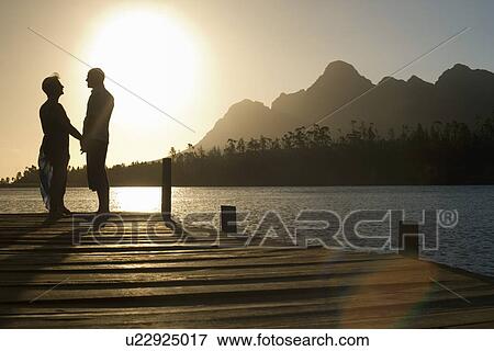 Couple standing on dock by lake holding hands side view. View Large Photo Image Stock Photo - Couple standing on dock by lake holding hands side view.. Fotosearch
