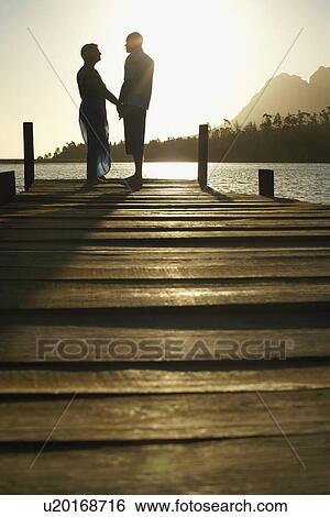 Couple standing on dock by lake holding hands side view. View Large Photo Image Stock Photograph - Couple standing on dock by lake holding hands side view.. Fotosearch