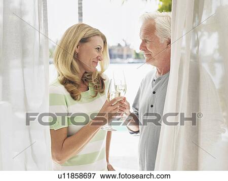 Couple toasting with champagne flutes standing behind curtain View Large Photo Image Stock Photo - Couple toasting with champagne flutes standing behind curtain. Fotosearch