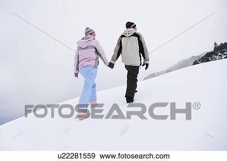 Couple walking up snow-covered hill back view low angle view View Large Photo Image Stock Photo - Couple walking up snow-covered hill back view low angle view. Fotosearch