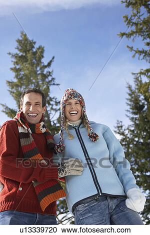 Stock Image - Couple wearing winter clothing standing on hillside low angle view portrait. Fotosearch