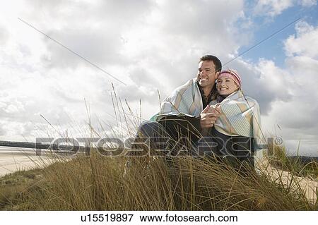 Stock Photo - Couple wrapped in blanket embracing at ocean. Fotosearch