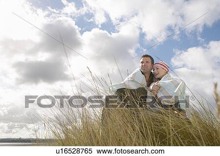Stock Photography - Couple wrapped in blanket embracing in grass. Fotosearch
