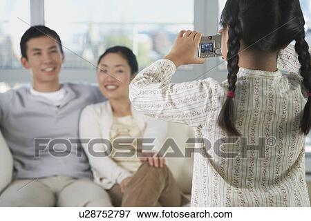 Stock Photo - Daughter taking picture of parents on sofa back view. Fotosearch