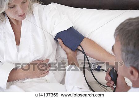 Stock Photo - Doctor using sphygomometer to check blood pressure of patient lying in bed. Fotosearch