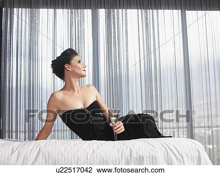 Stock Image - Elegant woman in black evening dress holding champagne flute. Fotosearch