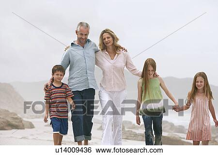 Stock Photograph - Family with three children (5-6 7-9 10-12) walking on beach. Fotosearch