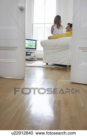 Stock Image - Father and daughter (5-6) watching cartoons in television back view. Fotosearch