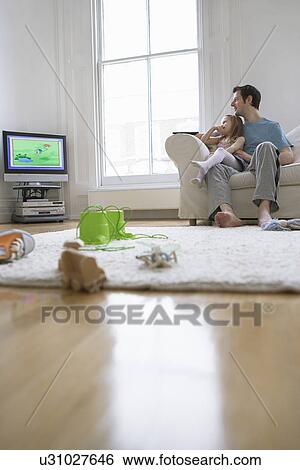 Stock Photograph - Father and daughter (5-6) watching match in television. Fotosearch