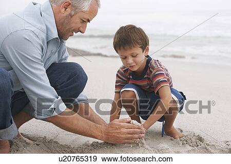 Stock Photo - Father and son (5-6) playing in sand on beach. Fotosearch