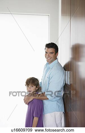 Stock Photo - Father and son (7-9) leaning on wardrobe and smiling. Fotosearch