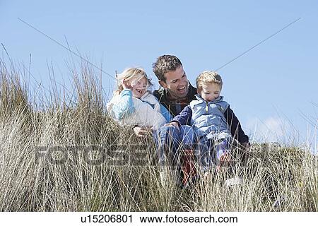 Stock Image - Father with two children (4-6) sitting in long grass. Fotosearch