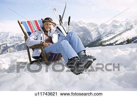 Stock Image - Female skier sitting on deckchair in mountains. Fotosearch