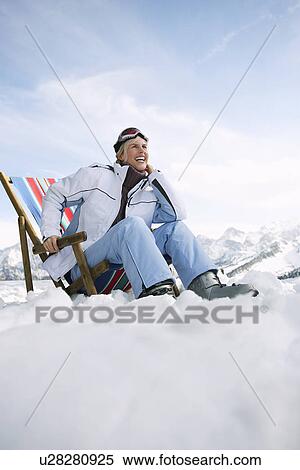 Stock Photography - Female skier sitting on deckchair in mountains low angle view. Fotosearch