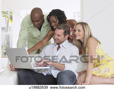 Stock Photo - Four adults on sofa looking at laptop. Fotosearch