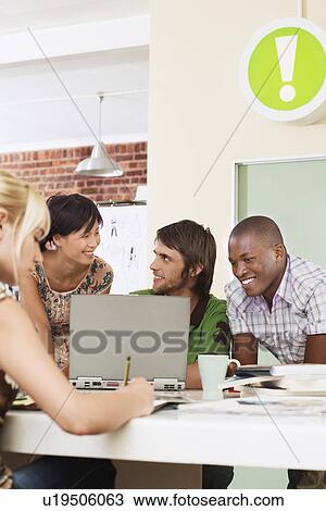 Stock Image - Four people having meeting around laptop.. Fotosearch