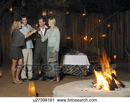 Stock Image - Four people toasting at outdoor nightclub near bonfire night. Fotosearch