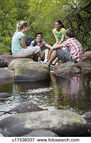 Four teenagers (16-17 years) sitting on stone by river talking View Large Photo Image Stock Photo - Four teenagers (16-17 years) sitting on stone by river talking. Fotosearch