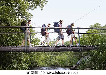 Four teenagers (16-17 years) backpacking in forest crossing wooden bridge side view View Large Photo Image Stock Photo - Four teenagers (16-17 years) backpacking in forest crossing wooden bridge side view. Fotosearch
