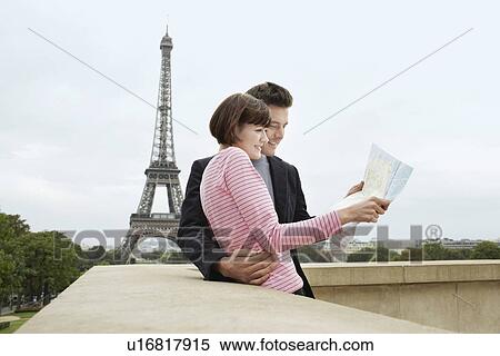 Stock Photography - France Paris Couple reading map on balcony in front of Eiffel Tower. Fotosearch