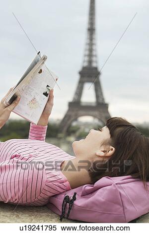 Stock Photography - France Paris Young woman reading book on balcony with Eiffel Tower in distance. Fotosearch