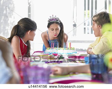 Stock Photograph - Girl (10-12) blowing out birthday candles at party. Fotosearch