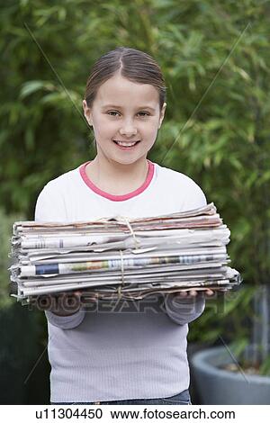 Stock Image - Girl (10-12) holding bundle of waste paper smiling. Fotosearch