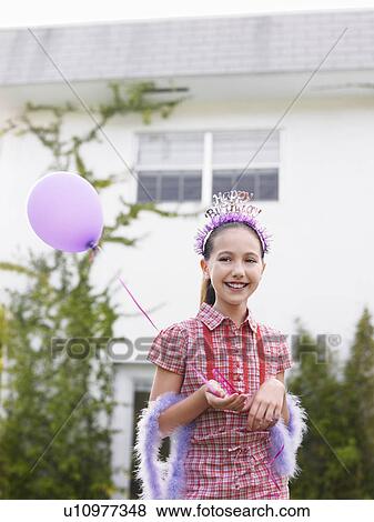 Stock Photo - Girl (10-12) in feather boa holding balloon outside house. Fotosearch