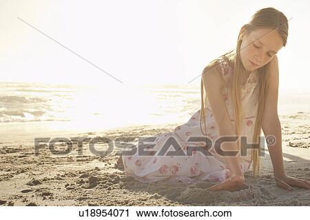 Stock Image - Girl (10-12) playing in sand on beach at sunset. Fotosearch