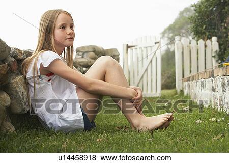 Stock Photo - Girl (10-12) sitting against wall in garden. Fotosearch