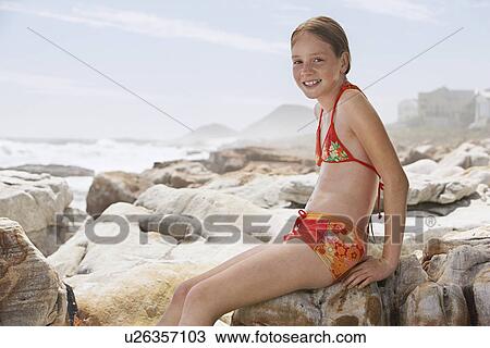 Stock Image - Girl (10-12) sitting on rock on beach portrait. Fotosearch