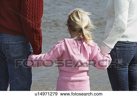 Girl (5-6) holding hands with parents at ocean View Large Photo Image Stock Photo - Girl (5-6) holding hands with parents at ocean. Fotosearch