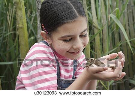 Stock Image - Girl (5-6) holding toad by reeds. Fotosearch