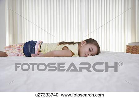 Stock Image - Girl (5-6) lying on bed. Fotosearch