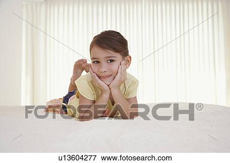 Stock Photo - Girl (5-6) lying on bed. Fotosearch