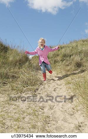 Picture - Girl (5-6) running down sand dunes. Fotosearch