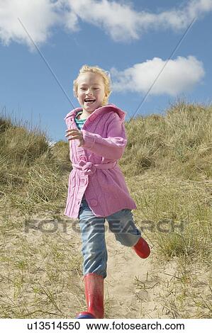 Stock Image - Girl (5-6) running down sand dunes. Fotosearch