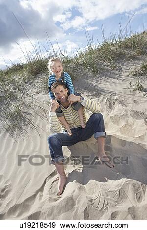 Stock Photo - Girl (5-6) sitting on father's shoulders on beach portrait. Fotosearch
