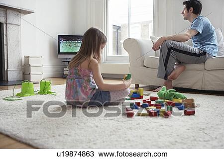 Girl (5-6) sitting on floor playing with blocks father watching television View Large Photo Image Stock Image - Girl (5-6) sitting on floor playing with blocks father watching television. Fotosearch