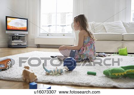 Stock Photo - Girl (5-6) sitting on floor surrounded with toys watching television. Fotosearch