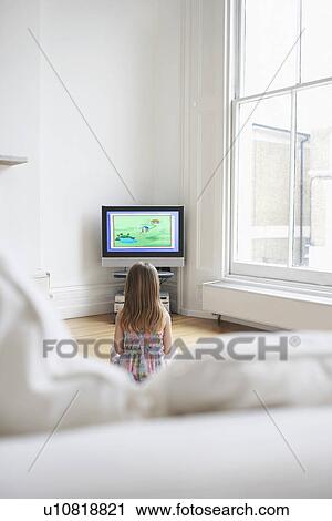 Stock Image - Girl (5-6) watching cartoons in television back view. Fotosearch