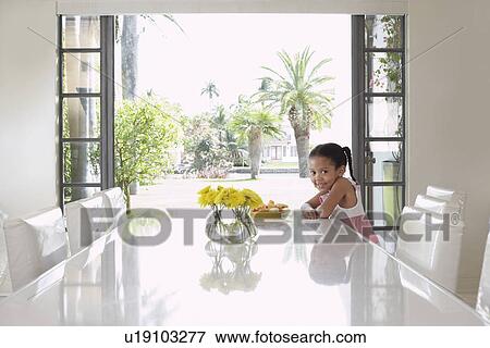 Stock Photo - Girl (5-6 years) sitting at dining table. Fotosearch
