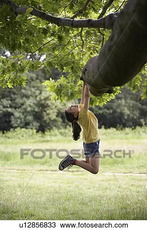 Stock Image - Girl (7-9) hanging from tree. Fotosearch