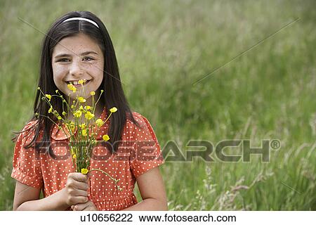 Stock Image - Girl (7-9) holding flowers in field portrait. Fotosearch