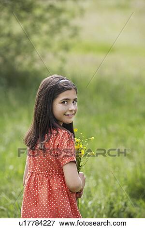 Stock Photo - Girl (7-9) holding flowers in field portrait. Fotosearch