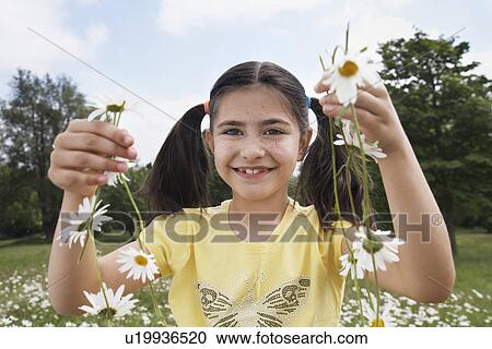 Stock Image - Girl (7-9) holding flowers in meadow portrait. Fotosearch