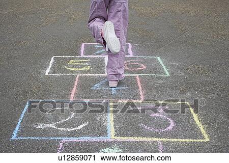 Stock Image - Girl (7-9) playing hop-scotch in school playground low section. Fotosearch