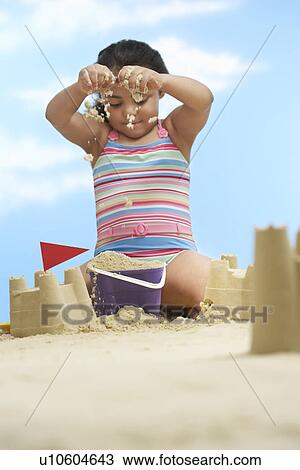 Stock Image - Girl (7-9 years) building sand castles on beach. Fotosearch