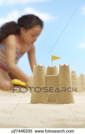 Stock Photography - Girl (7-9 years) building sand castles on beach focus on sand castle in foreground. Fotosearch